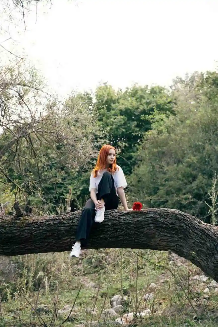 Young woman sitting on a tree branch in nature, wearing casual denim jeans