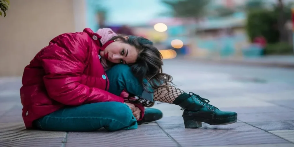 A stylish woman wearing a red hoodie and Vervet jeans, sitting outdoors, showcasing the trendy and casual style of Vervet denim paired with bold outerwear