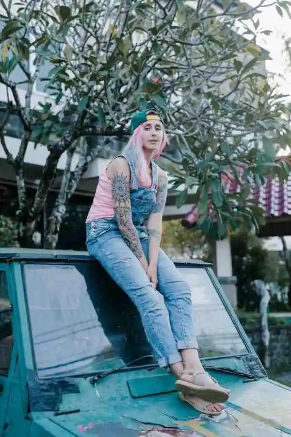 "Young woman wearing distressed flare jeans and a pink top, sitting on a car hood. Showcasing a casual, edgy look with women's flare jeans and street-style fashion