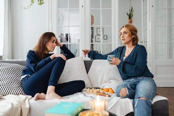  Two women in cozy outfits discussing fashion on a couch, emphasizing the importance of tummy control jeans for a flattering fit and comfort