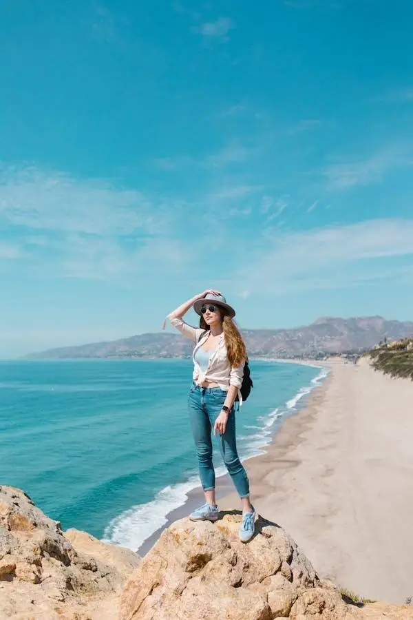 "Woman wearing Flying Monkey jeans standing on a cliff by the beach, showcasing the perfect blend of comfort and style for outdoor adventures."