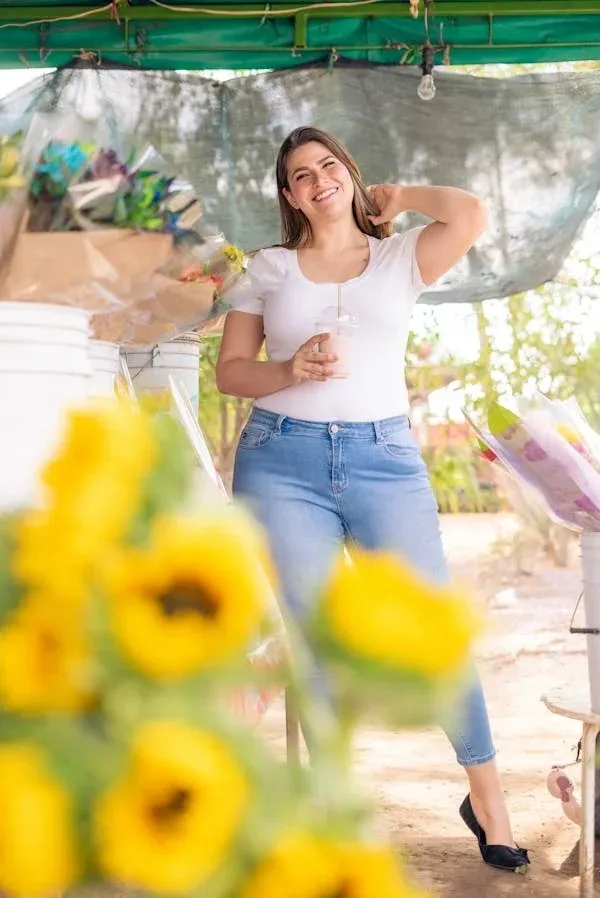 "Smiling woman wearing high-waisted Flying Monkey jeans, standing near sunflowers at a market. Perfect fit showcases accurate sizing and comfort in Flying Monkey jeans, a trusted brand for stylish, well-fitting denim."