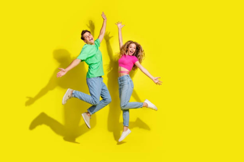 Two people happily jumping, both wearing casual outfits with relaxed-fit boyfriend jeans against a bright yellow background, showcasing the laid-back style of boyfriend jeans.