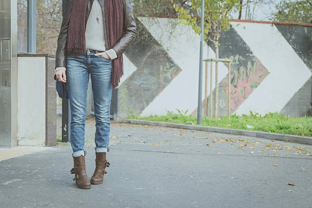 Woman wearing black knee-high boots with white straight-leg jeans and a black jacket, standing outdoors in a casual yet stylish look.