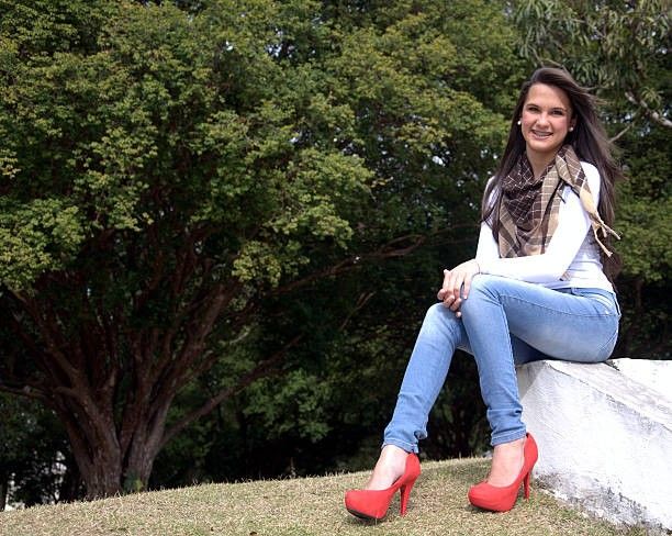 Woman sitting outdoors wearing blue skinny jeans and red high-heeled boots, showcasing a fun and playful boot style with vibrant color choices like pinky boots.