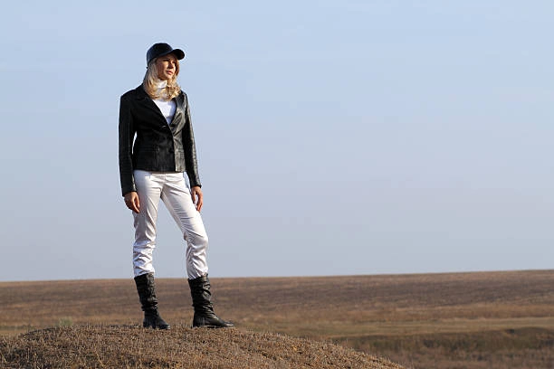 Woman wearing black knee-high boots with white straight-leg jeans and a black jacket, standing outdoors in a casual yet stylish look.