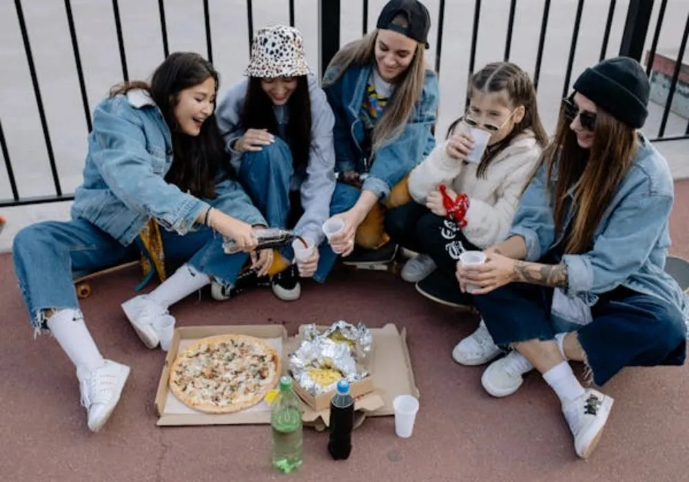 Group of friends in casual denim outfits enjoying pizza while showcasing how to effortlessly style cropped wide leg jeans for a relaxed, trendy look.