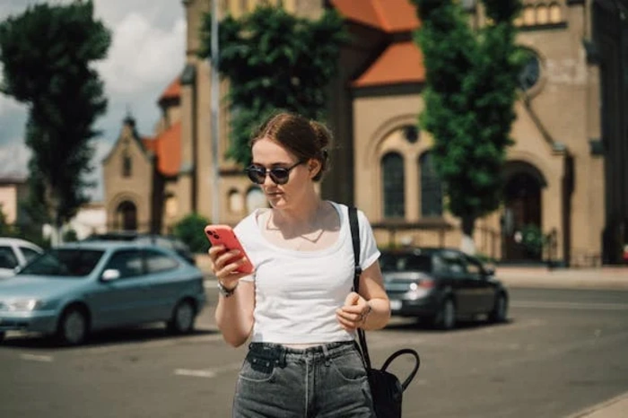 woman wearing low-rise denim jeans and a casual white t-shirt while checking her phone outdoors, showcasing a versatile, laid-back look suitable for different occasions.