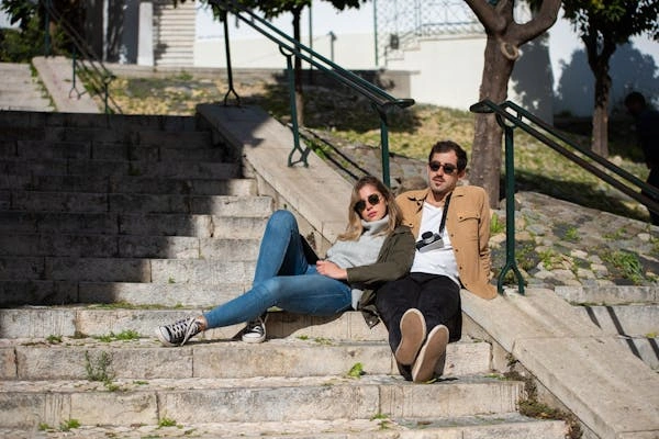 A couple relaxing on outdoor stairs, with the woman wearing mid-rise jeans styled casually with sneakers and a jacket, perfect for various casual occasions.