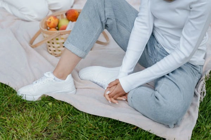 Smiling woman sitting on a grassy pasture wearing casual low-rise jeans and a cozy sweatshirt, with a sheep grazing behind her. The relaxed, nature-inspired setting highlights the comfort and versatility of low-rise jeans for an effortless outdoor look