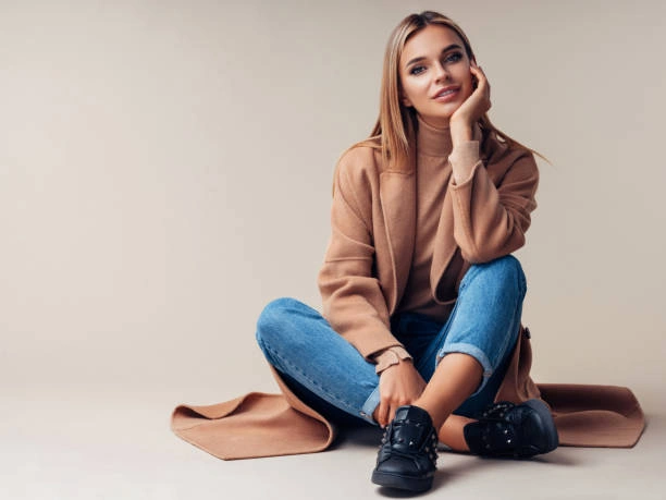 Stylish woman wearing medium wash jeans paired with a camel coat, turtleneck sweater, and black sneakers, showcasing the versatility and popularity of medium wash denim for creating chic, layered looks perfect for casual outings.