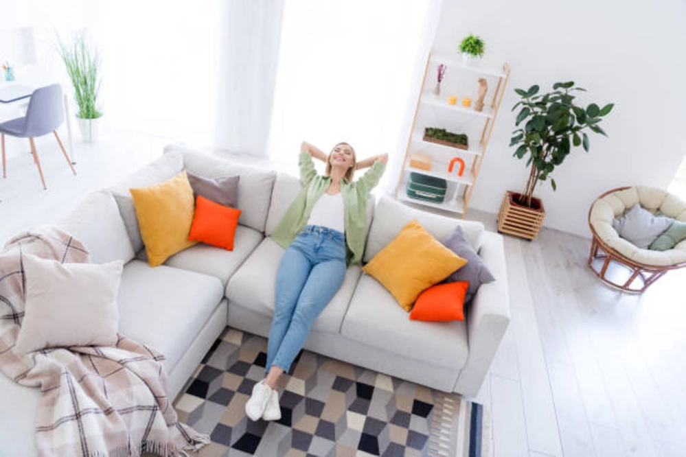 Relaxed woman wearing stylish Vervet jeans, known for their comfort and trendy designs, lounging on a modern, cozy sofa in a bright, well-decorated living room